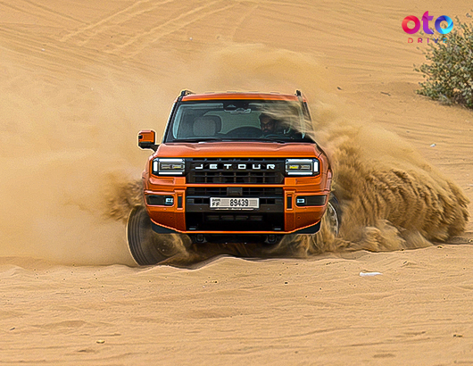 Orange Jetour G700 SUV drifting powerfully through desert sand dunes kicking up dust.